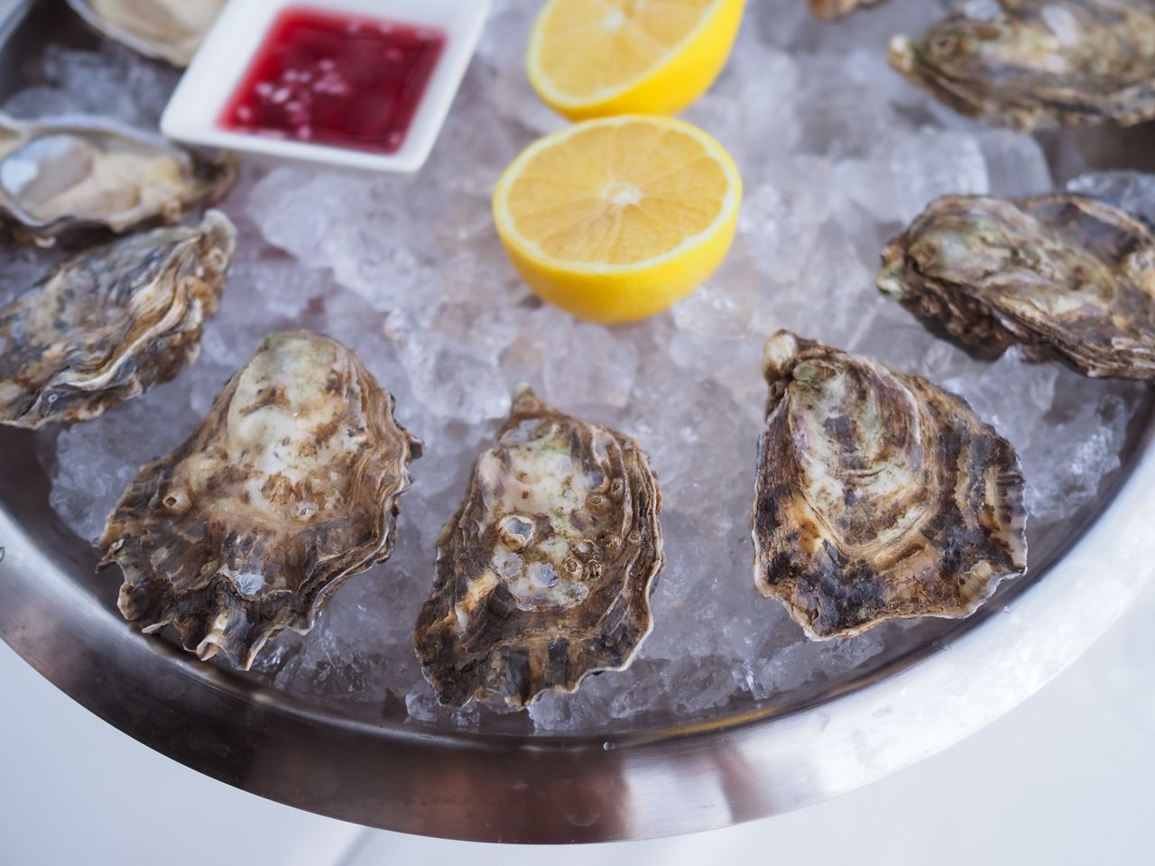 About A gourmet seafood platter of fresh oysters served on ice with lemon and sauce.