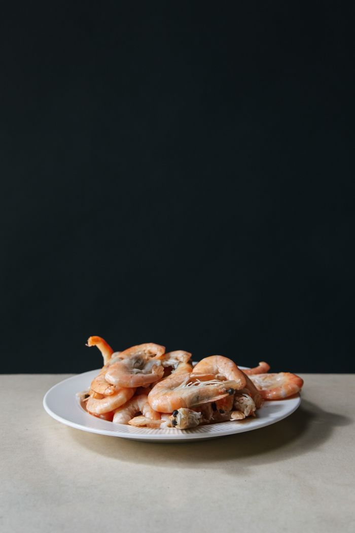 About A minimalist still life of fresh shrimps served on a white plate against a dark backdrop.